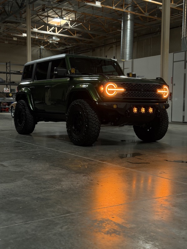 Green Ford Bronco with lit halo headlights on the shop floor